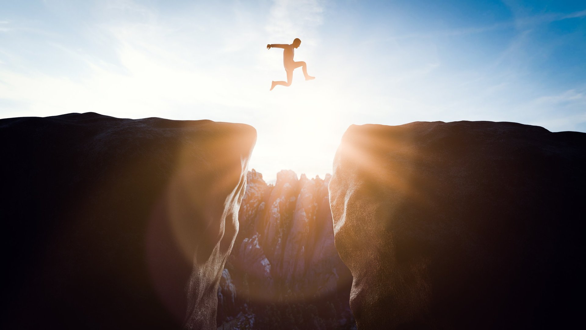 Man jumping over a gap between rocks at sunset